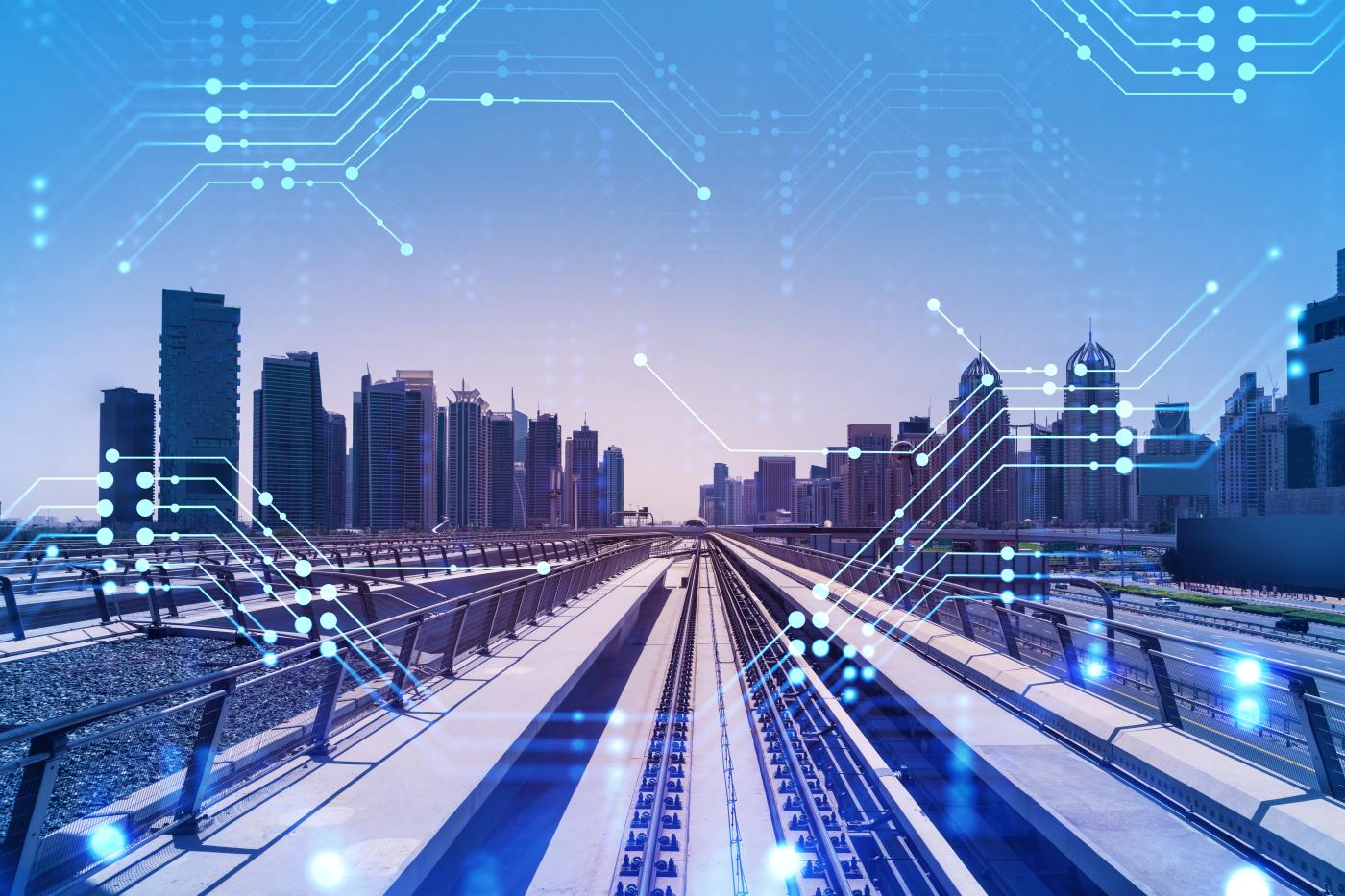 A photo of train tracks leading toward a city is overlaid with circuit board symbols. 